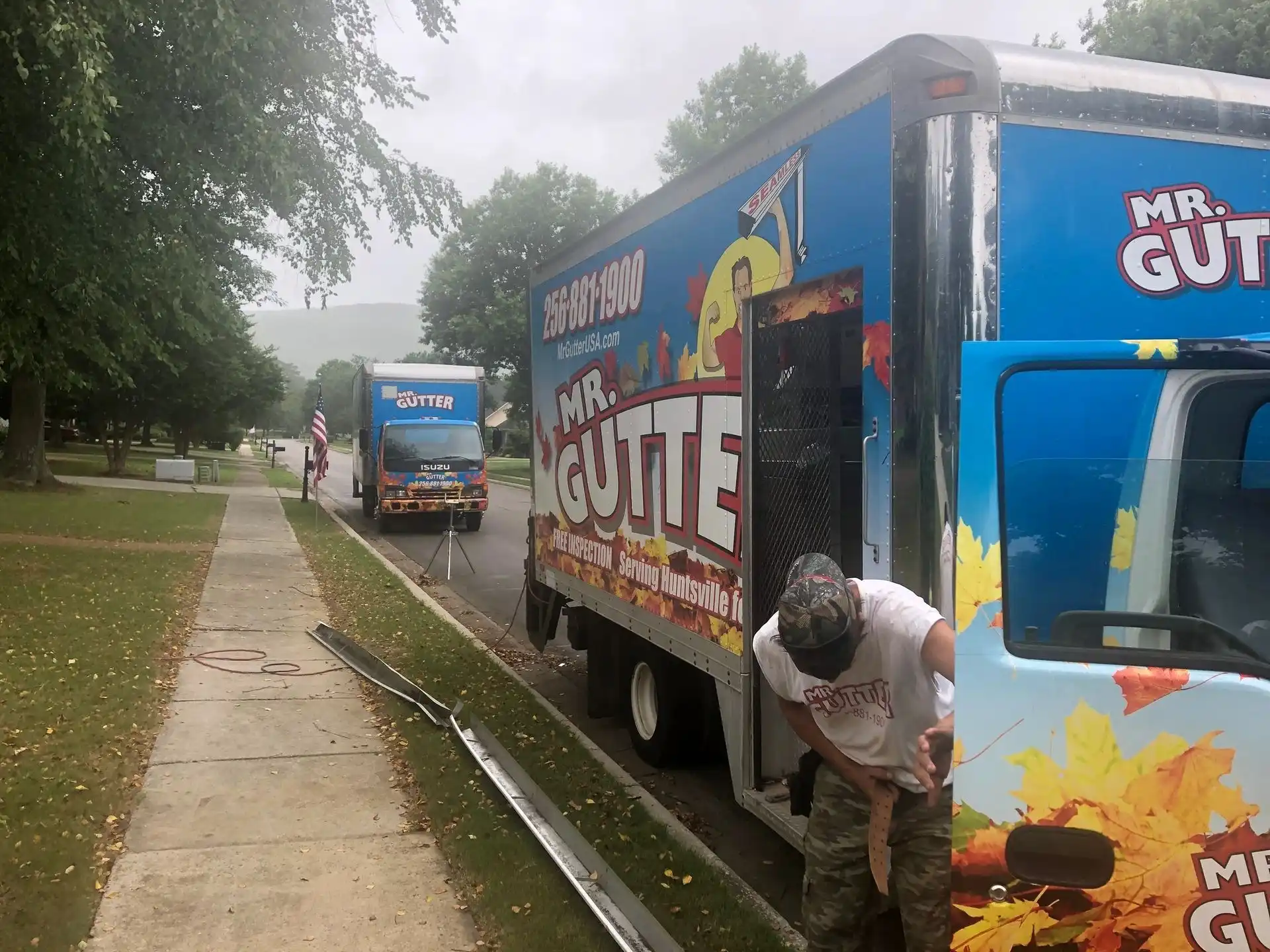 Worker stepping out of a Mr Gutter panel truck with another service truck parked behind in Madison, AL